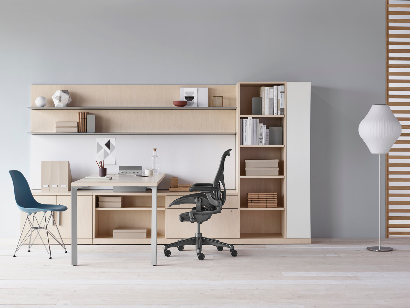 A Canvas Private Office with light wood storage, upper shelves, black Aeron chair, and blue Eames Molded Plastic side chair.