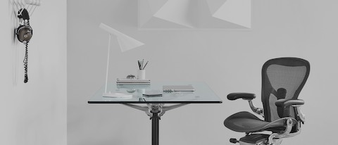 A square Burdick table with a glass top, used as a desk and complemented by a black Aeron office chair.