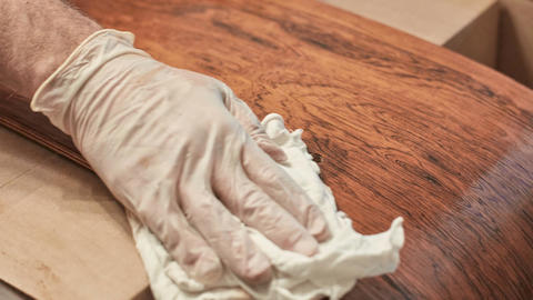 A worker with a gloved hand rubs oil on the Santos Palisander shell of an Eames Lounge Chair.