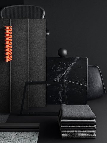 Stacks of folded gray, black, muted patterned textile samples on a dark gray table, with a black Metaform collaborative space wall behind them.