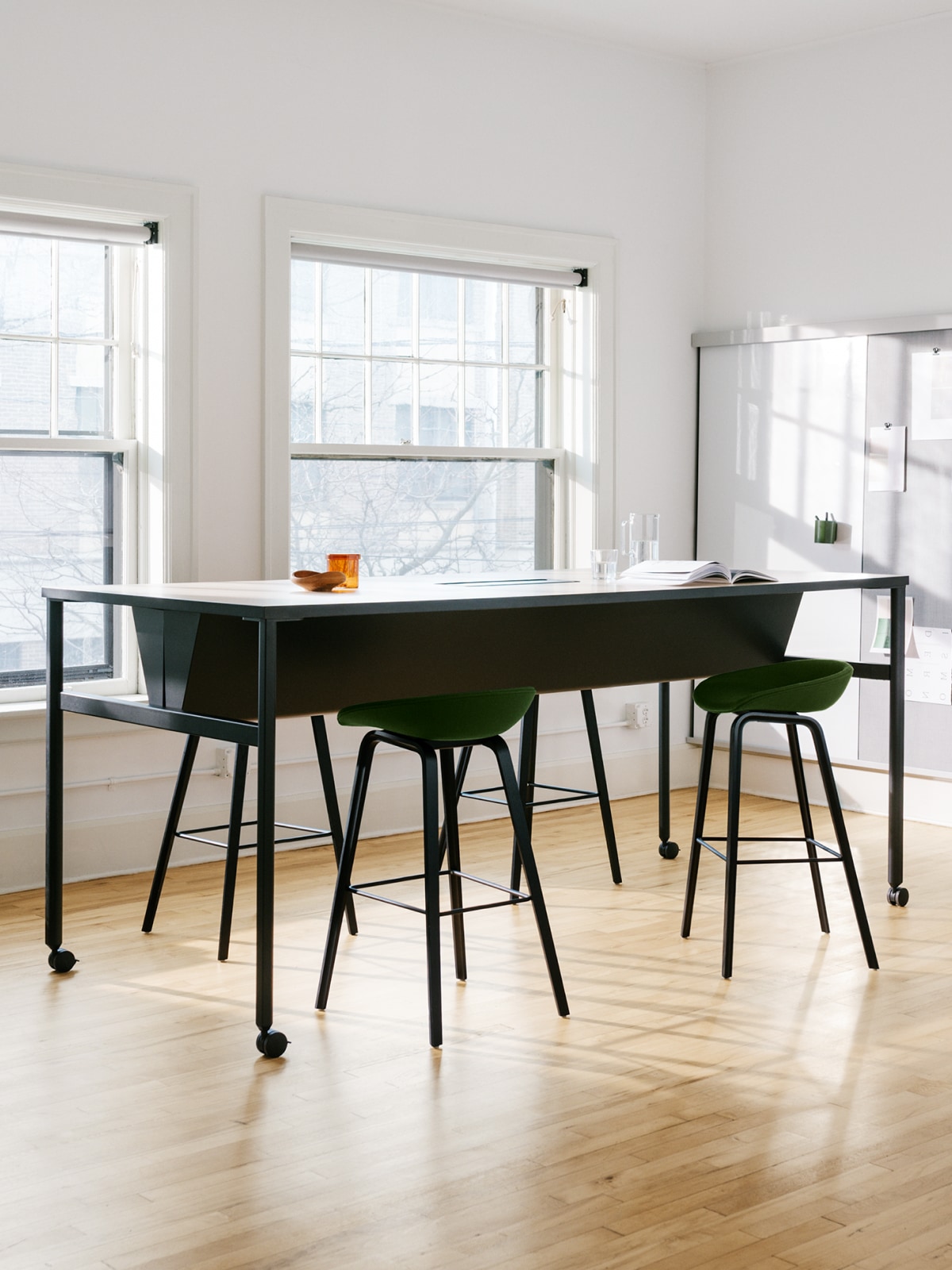 Ein schwarzer, beidseitiger OE1 Communal Table auf Rollen sowie eine OE1 Wall Rail und ein Board im Hintergrund eines großen, hellen Konferenzraums.