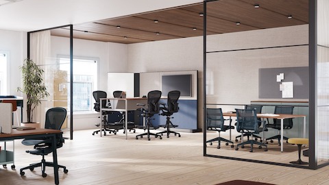 A collaborative space featuring four Aeron stools in dark gray around a table with monitor and four Setu chairs around a meeting table.