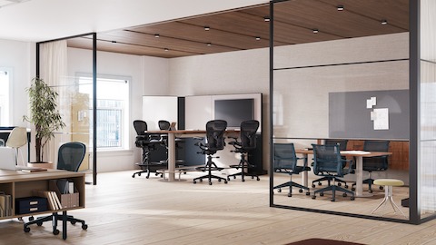 A collaborative space featuring four Aeron stools in dark gray around a table with monitor and four Setu chairs around a meeting table.