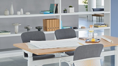 Un espace de réunion ouvert avec une table Atlas Office Landscape réglable en hauteur et trois chaises Keyn grises.