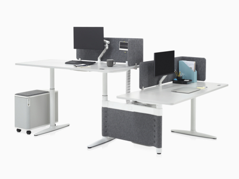 Height-adjustable Atlas Office Landscape desks in a 90-degree configuration, one at standing height and one at seated height.