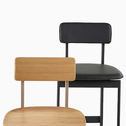 A close-up of an oak Betwixt Stool with a black leather version behind it.