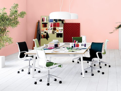 A collaborative space with blue and green Setu Chairs around a Canvas Office Landscape table holding fabric and material samples.