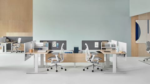 Canvas Vista workstations in light wood and white with gray Mirra 2 office chairs and a conference room with a gray Cosm office chair in the background.