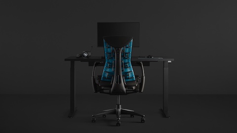 A full gaming setup with an Embody Gaming Chair pulled up to the Motia Gaming Desk with an Ollin Monitor Arm on top of it, all on a black background.