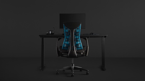 A full gaming setup with an Embody Gaming Chair pulled up to the Nevi Gaming Desk with an Ollin Monitor Arm on top of it, all on a black background.