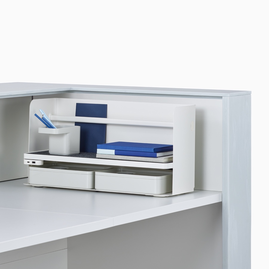 A close-up view of an Ubi Organizer and Formwork in the corner of the work surface within Commend Nurses Station organizing a few notebooks and pens.