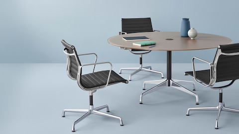 Three black Eames Aluminum Group mid-back chairs surround a round Eames Table.