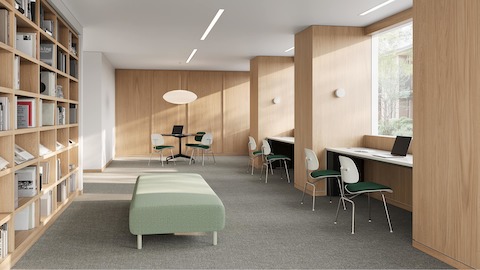 Library with oak bookshelves and desks with the green upholstered Eames EC-127 chair with a white shell and metal frame.