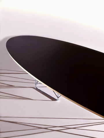 Close view of an Eames Wire Base Elliptical Table with a black top, focusing on the beveled edge. 