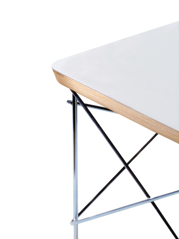 Partial view of a white Eames Wire Base Low Table, focusing on the welded wire rods and beveled top edge. 