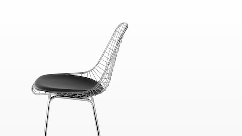 Upper half of a silver Eames Wire Stool with a black seat pad, viewed from the side. 