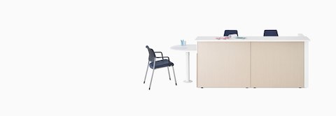 Ethospace Nurses Station in a light wood finish with transaction surface and ADA peninsula surface in white, a Verus Side Chair in blue, and Sayl Chairs in blue.