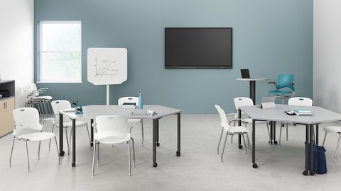 Zwei Paare weißer, trapezoider Everywhere Tables, arrangiert in einer Lernumgebung, mit weißen Caper Stapelstühlen.