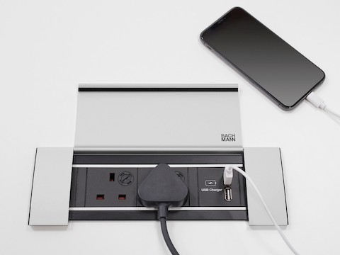 Eine offene Abdeckung am Stromversorgungsrahmen, mit Stromstecker und einem angeschlossenen Mobiltelefon.