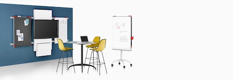 A collaboration space featuring a table, media tile, and display boards from Exclave, as well as three yellow stools.