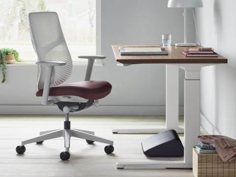 A side view of black Foot Pillow, under a Renew Sit-to-Stand Table with a Verus Chair.