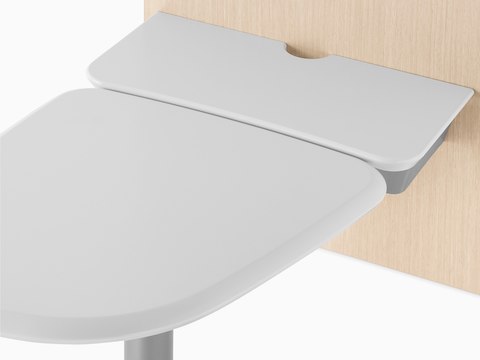 A close-up view of an Intent Solution wall unit in a light wood finish with a mobile, height-adjustable table in white.