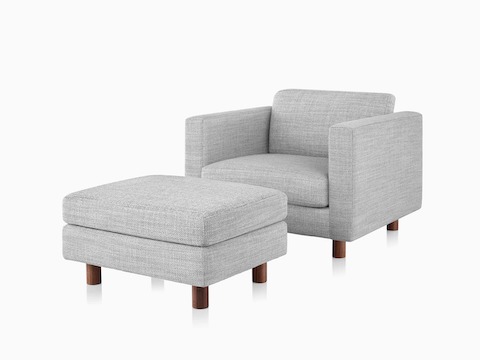 Una seduta lounge e un ottoman Lispenard con imbottiture in tessuto grigio e gambe in legno di noce, vista frontale angolare.