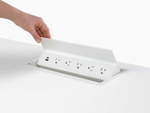 Hand opening an embedded table power source with USB-A port, USB-C port, and five A/C power outlets.