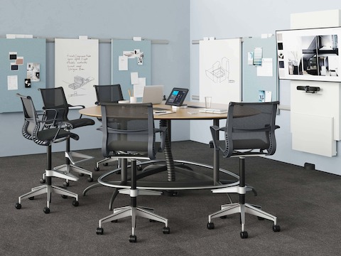 A meeting space featuring an Exclave table with five black Setu Stools. The table is connected to power and data by a Logic Reach Wall Start and Electrical Hub.