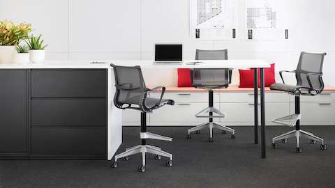 Black and white Meridian Storage collaborative setting with three gray Setu stools and white Meridian lateral files with light orange cushion tops in the background.