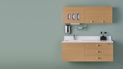 Wall-mounted Mora System clinical casework, including drawers, a sink, overhead cabinets, and a glove dispenser.