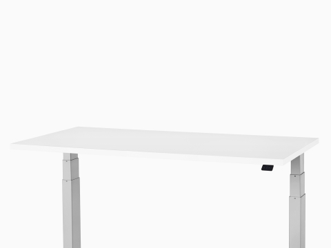 Viewed at an angle, a Nevi Sit-to-Stand Table, with a white work surface and metallic silver T-leg base at a standing height.