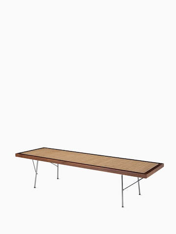 A Nelson Cane Bench with a walnut frame and metal legs, viewed from the side at an angle. Select to go to the Nelson Cane Bench product page. 