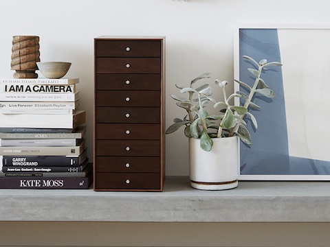 A vertical nine-drawer Nelson Miniature Chest with no base sits next to a stack of books on a shelf.