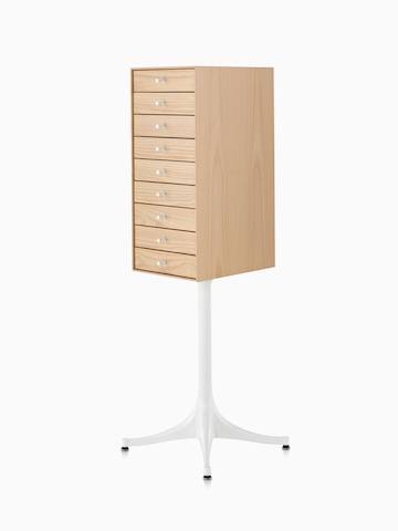 Angled view of a vertical nine-drawer Nelson Miniature Chest with a light finish and white pedestal base. 