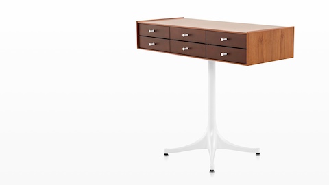 Angled view of a horizontal six-drawer Nelson Miniature Chest with a medium finish and white pedestal base. 