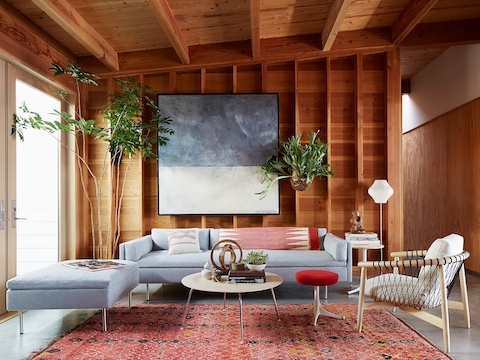 A residential living area featuring a light gray Bolster sofa and a Nelson Pedestal Stool with a red upholstered seat.