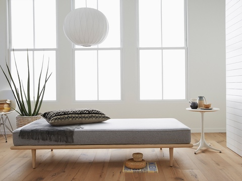 A white Nelson Pedestal Table serves as a convenient bedside surface for a gray Nelson Daybed. 