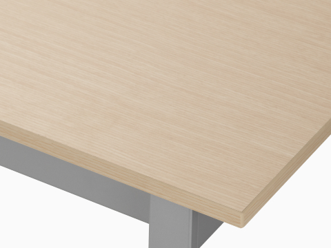 Detail of the top of an Easton table with a clear on ash laminate top and metallic silver trim.