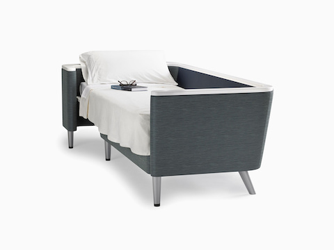 A Nemschoff Palisade Flop sofa converted to sleep surface in dark gray textile with white solid surface arms caps and white pillow and sheet.