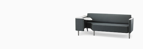 A Nemschoff Palisade Flop sofa in dark gray textile with white solid surface arms caps and white adjustable table with Durawrap top.
