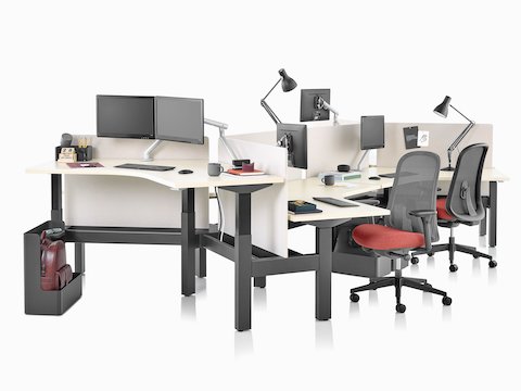 Escritorio elevado Nevi Link con patas negras y superficies de trabajo de 120 grados, sillas para oficinas Lino en rojo y negro y pantallas en blanco. Dos de los seis escritorios están elevados a altura de pie.
