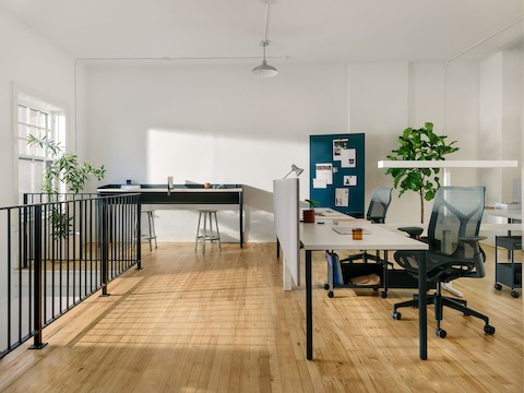 White OE1 Rectangular Tables in a workstations configuration, with a blue OE1 Communal Table and blue OE1 Mobile Easel and project board in the background.