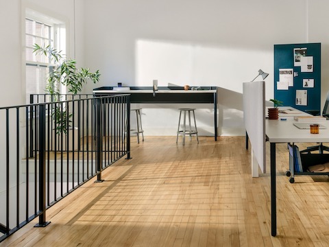 White OE1 Rectangular Tables in a workstations configuration, with a blue OE1 Communal Table and blue OE1 Mobile Easel and project board in the background.