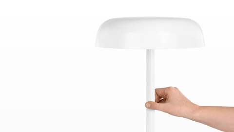 A hand touches the stem of a white Ode Lamp to turn it on or off.