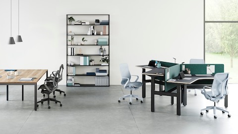 Ambiente de escritório aberto com um conjunto de 3 mesas Ratio 120 posicionadas em alturas variadas à direita e uma mesa Layout grande à esquerda. Uma seleção de cadeiras Cosm com encostos altos e baixos posicionadas ao redor de mesas com uma estante ao fundo.