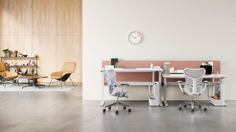 Configuração de escritório com um par de mesas Ratio ao fundo com superfícies de trabalho retangulares em cadeiras Mirra 2 cinzas e uma área de lounge com cadeiras de concha única Eames e estante ao fundo. Uma das mesas está levantada até a altura para trabalhar em pé.