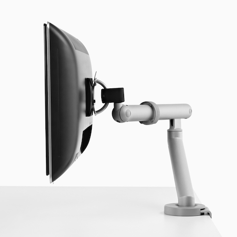 A close-up view of a Renew Link standing desk system's computer monitor supported by a silver Flo Monitor Arm.