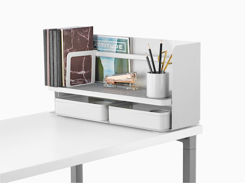 Een kleine witte Ubi-desktoporganizer met een grijze antislipplank bevat boeken, een nietmachine, een potloodbeker en twee opslagdozen.
