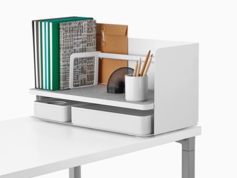 Een grote witte Ubi-desktoporganizer met een grijze antislipplank bevat boeken, een potloodbeker en twee opbergdozen.